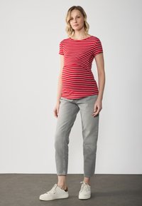 Top de maternidad a rayas rojas y blancas con mangas cortas, combinado con jeans tapered gris claro y zapatillas blancas. Diseño simple, material suave.