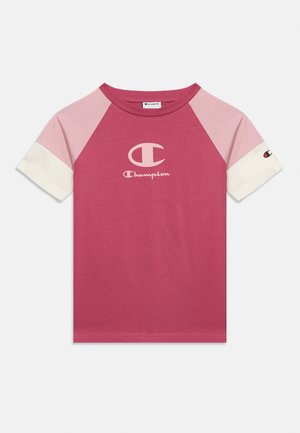 T-shirt raglan à manches courtes avec corps rose, épaules rose clair, poignets blancs aux manches et logo Champion sur la poitrine et la manche.