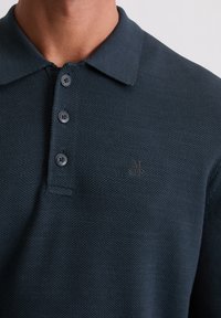 Dunkelblaues Polohemd aus strukturiertem Strickstoff mit klassischem Kragen und drei Knöpfen, versehen mit einem dezenten Logo in der oberen linken Ecke.