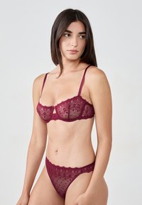 Bordowy komplet bielizny z koronkowym biustonoszem i dopasowanymi figami, charakteryzujący się misternymi wzorami, kokardkowymi akcentami, regulowanymi ramiączkami oraz falbaniastymi krawędziami.