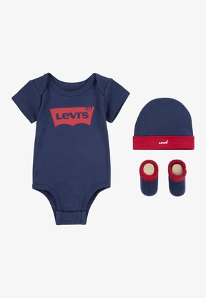Navy katoenen rompertje met het rode Levi's-logo, bijpassende navy pet met rode rand, en navy babysokjes met rode bies en beige zolen.