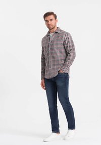 Camicia a quadri nei toni del rosso, blu e bianco, abbinata a jeans blu scuro e sneakers bianche. Colletto semplice e vestibilità casual.