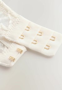 Spallina di pizzo bianco con una banda elastica texturizzata e chiusure ad uncino e occhiello in metallo dorato; presenta una finitura liscia e bordi morbidi.