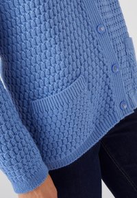 Cardigan blu con texture, caratterizzato da un motivo a nido d'ape, polsini e orlo a coste, e due tasche frontali con chiusura a bottone.