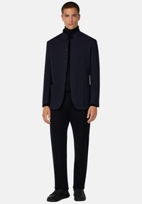 Chaqueta de marinero ajustada con un alto cuello, cierre de cuatro botones y dos bolsillos frontales, combinada con pantalones negros y zapatillas negras.