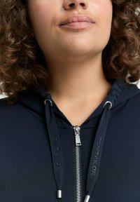 Sudadera azul oscura con cremallera en el frente, cuerdas ajustables con texto en relieve y una textura de tela suave.