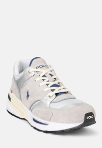 Šedé semišové tenisky se stříbrnými akcenty, текстurovanou síťovinou, námořnickými tkaničkami a bílou podrážkou. Obsahují logo na boční straně a vzadu.