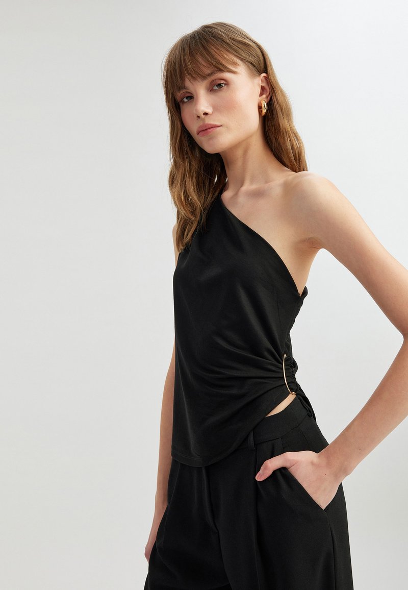 Haut noir à une épaule en tissu doux, avec un détail noué sur le côté et un accent circulaire. Design minimaliste avec une coupe décontractée.