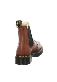 Botín de piel marrón con un suave forro crema, paneles laterales elásticos, suela gruesa de goma negra y detalle de costura amarilla en la suela.