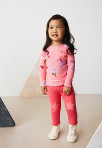 Chemise rose à manches longues avec des motifs floraux et hippiques ; leggings roses avec des appliqués en forme d'étoile. Les deux ont une texture douce et un design décontracté.