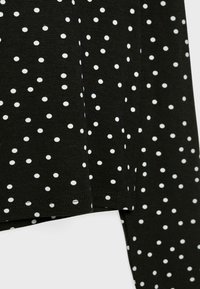 Schwarzes Langarmshirt mit gleichmäßig verteilten weißen Tupfen, mit glatter Textur und abgerundetem Saum.
