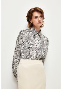 Button-Down-Bluse im weißen und schwarzen Tierdruck mit Kragen, langen Ärmeln und lockerer Passform. Kombiniert mit einem cremefarbenen Rock.