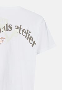 Hvid bomulds T-shirt med et buet grafisk design, der har teksten "ails atelier" i mørkegrå og orange accenter. Korte ærmer.