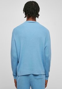 Ljusblå tröja med ribbat mönster, långa ärmar och rund halsringning, med en något lös passform och rak fåll.