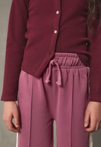 Bourgognefarvet ribstrikket cardigan med knapper og lyserøde joggingbukser med elastik i taljen og snøre, der har en glat tekstur.