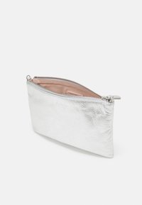 Hopeinen metallinhohtoinen nahkakuori, jossa on teksturoitu pinta, vetoketjukiinnitys ja vaaleanpunainen sisus, joka esittelee minimalismia ja ohutta profiilia.