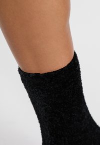 Czarna, puszysta skarpeta z rypsowym brzegiem, o miękkiej fakturze i dopasowanym kroju, zaprojektowana tak, aby zakrywać kostkę i część łydki.