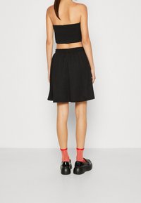 Svart kort topp och kjol, elastisk midja, mjukt tyg, kombinerad med svarta skor och röda knästrumpor. Minimalistisk design, inga mönster.