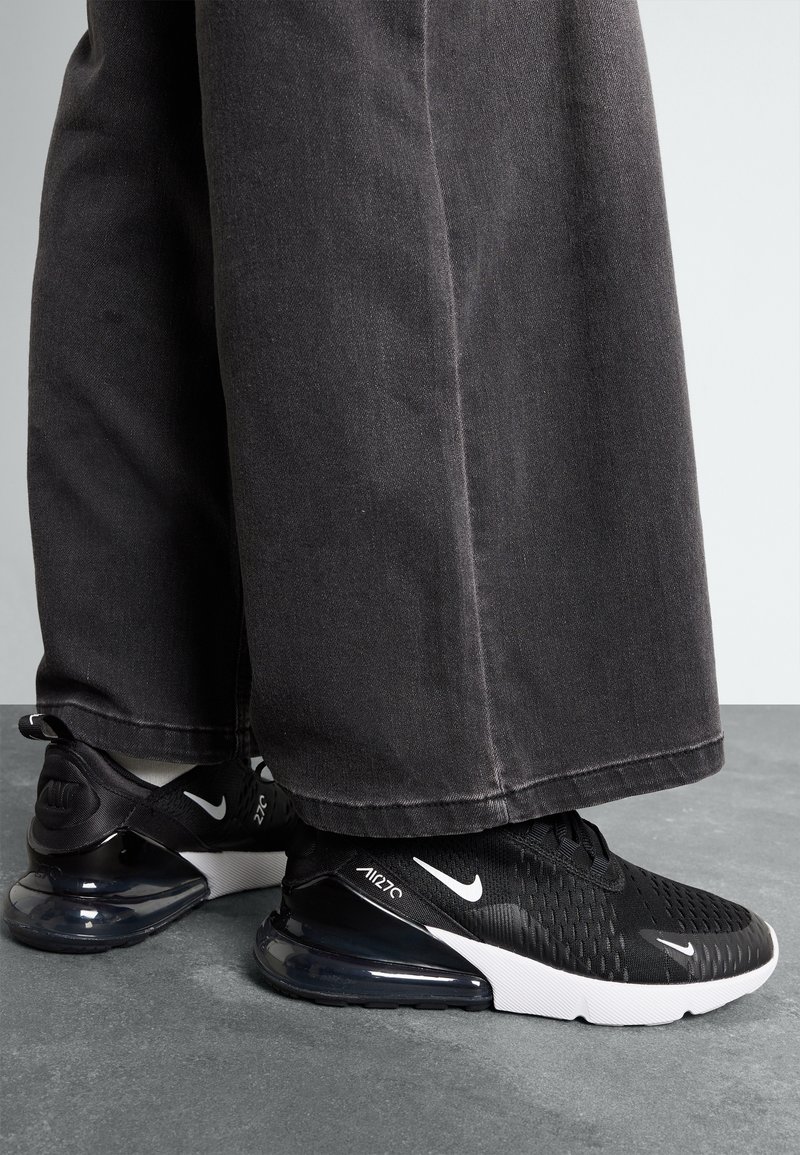 Black Nike Air Max 270 sneakers with a textured upper, white accents, and a transparent air cushioning unit, paired with dark wide-leg trousers.