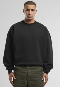 Felpa nera con scollo rotondo, vestibilità ampia e maniche lunghe, realizzata in un tessuto liscio. Abbinata a pantaloni cargo verde oliva.