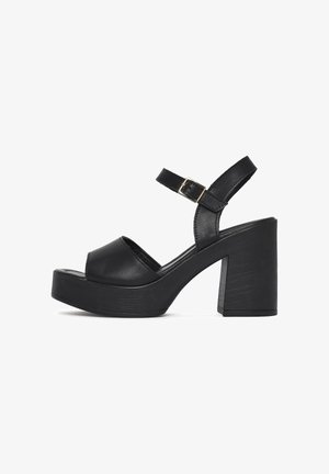 Black platform sandal with thick block heel, open toe, and ankle strap with silver buckle on white background.