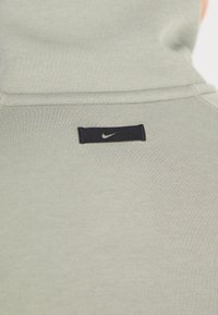 Ljusgrå sweatshirt med en slät textur, prydd med en svart Nike-logotyp sydd på baksidan. Enkelt design, utan mönster eller accenter.