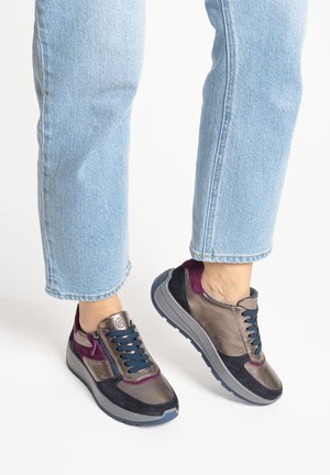 Feet wearing metallic, navy, and purple lace-up sneakers paired with light blue cropped jeans against a white background.