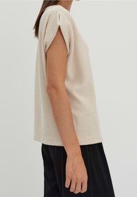 Beige ribbat kortärmad topp med avslappnad passform och uppvikta ärmar, tillsammans med svarta lösa byxor. Mjuk textur och avslappnad design.