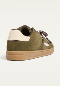 Baskets en daim vert olive avec un accent en cuir beige au talon, semelle en gomme texturée et lacets à motifs foncés.