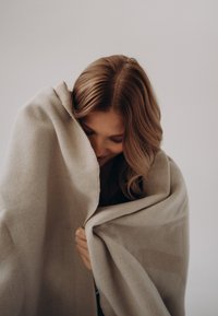 Couverture beige douce drapée sur les épaules, présentant une texture lisse et un motif subtil. Le matériau semble confortable et chaud.