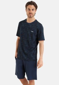 T-shirt bleu marine à manches courtes avec un motif de feuilles, col rond et détail de logo. Associé à un short bleu marine uni. Tissu doux et coupe décontractée.