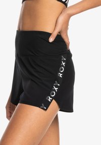 Zwarte sportshorts met een hoge tailleband, voorzien van een zijsplits en "ROXY"-branding in het wit langs de rand. Zacht, rekbaar materiaal.