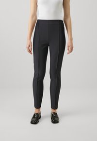 Leggings noirs taille haute au design épuré, avec des coutures verticales et des accents de zip à l'ourlet. Tissu lisse et extensible.