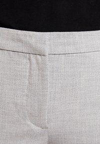 Pantalons gris clair en tissu lisse et texturé. Dotés de couturestailleur, d'une coupe droite et d'une taille plate. Pas de poches visibles.
