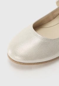 Metallisk silverfärgad balettflat med rund tå, slät yta och en beige sula. Har en enkel sydd kant runt öppningen.