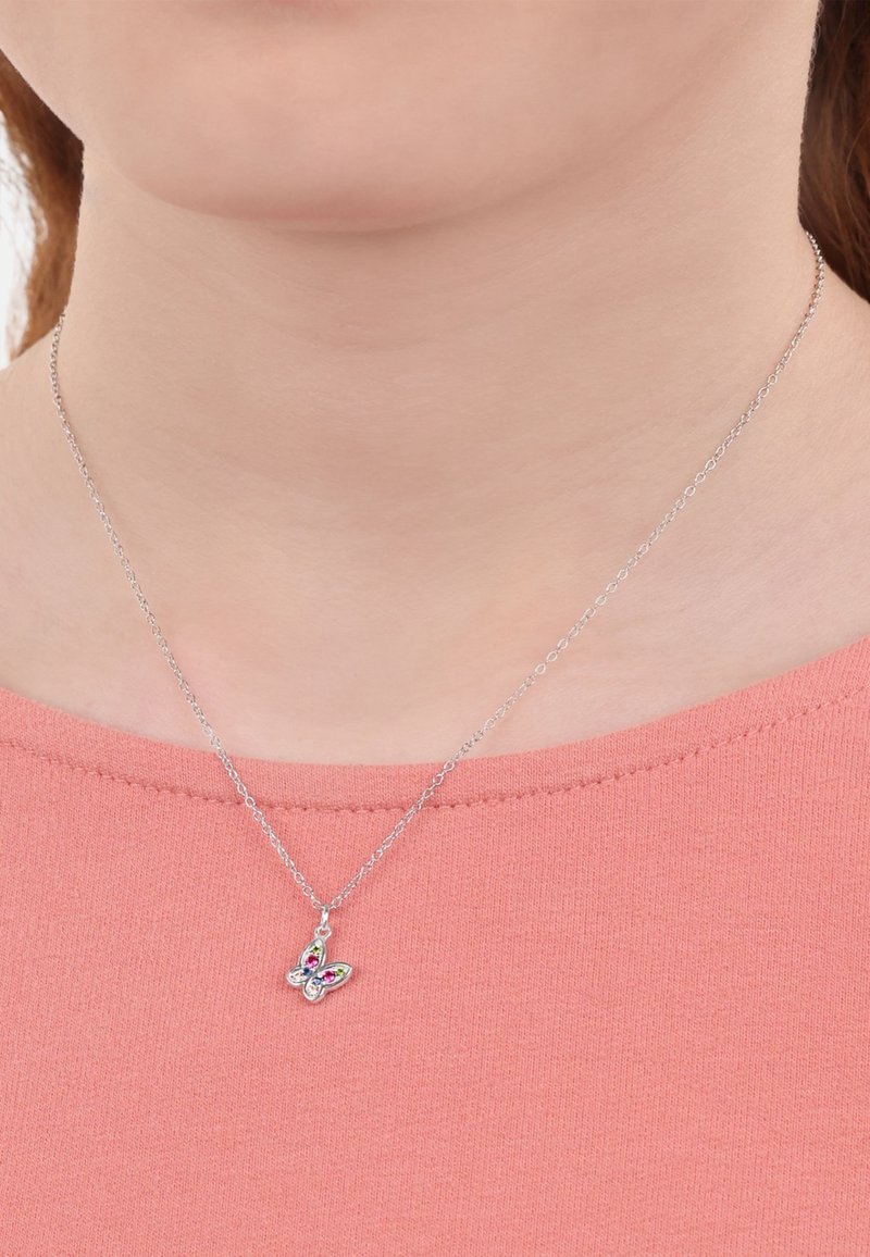 Collana con pendente a forma di farfalla in argento, con pietre preziose colorate, sospesa su una delicata catena, indossata su una morbida maglietta corallo.