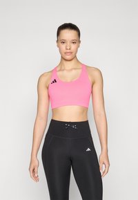 Rosa sports-bh med rund hals og sort Adidas-logo til venstre, sammen med højtaljede sorte leggings med en dekorativ sløjfe.