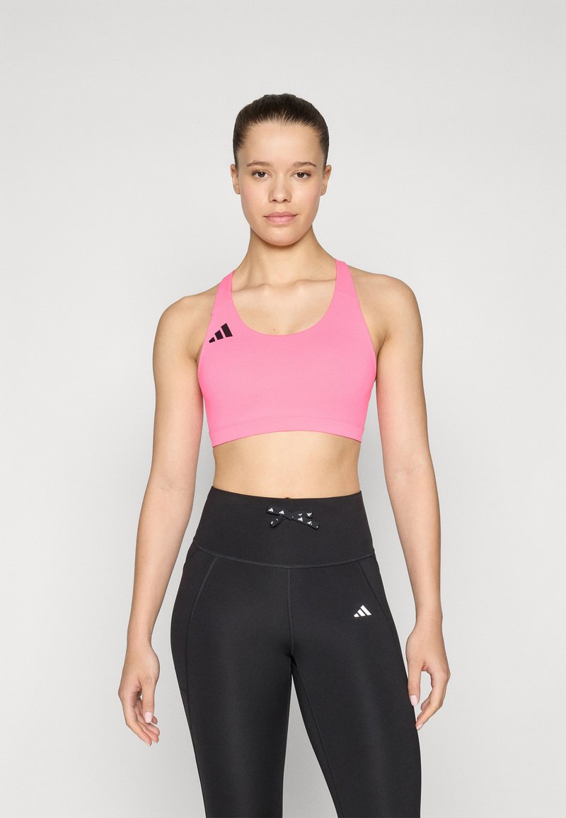 Rosa sports-bh med rund hals og sort Adidas-logo til venstre, sammen med højtaljede sorte leggings med en dekorativ sløjfe.
