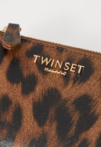 Ruskean ja mustan leopardi-kuosiset kangaspussit, joissa on kultainen logo "TWINSET MILANO" ja kultainen vetoketju. Sileä pinta, pyöristetty vetoketjun vetonauha.