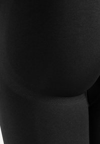 Close-up van een persoon die strakke zwarte leggings draagt, met de nadruk op de pasvorm en textuur van de stof rond de heup en bovenbeen.