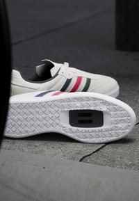 Białe sneakersy z trzema wzorzystymi paskami w kolorze różowym, granatowym i zielonym. Posiadają teksturowaną gumową podeszwę oraz gładką skórzaną cholewkę.