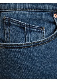Detalle del bolsillo de unos vaqueros de mezclilla en denim azul con costuras visibles y un pequeño bolsillo para monedas, que presenta un remache de cobre en el costado.