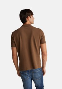 Hnědá polo košile s krátkým rukávem a hladkým povrchem, s klasickým límečkem a rovnými lemy, kombinovaná s modrými džíny.