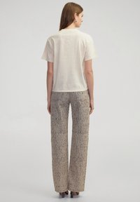 Camiseta corta de manga corta en color crema con un corte relajado, combinada con unos pantalones beige de pierna ancha que presentan un sutil patrón de manchas oscuras.