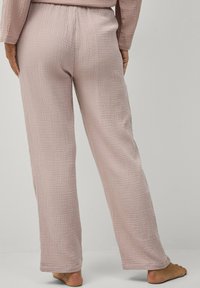 Lichtroze, gestructureerde, broek met wijde pijpen en een elastische tailleband. De stof heeft een ruitpatroon en een zachte, ademende kwaliteit.