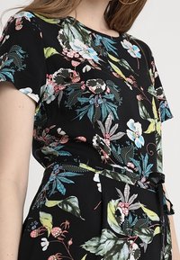 Vestido negro con flores que presenta patrones vibrantes en azul, rosa y verde, con mangas cortas y un cinturón en la cintura, confeccionado en una textura de tela ligera.