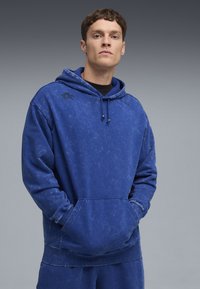 Blå p men's hoodie i mjukt material, med känguruficka, dragsko på huvan och diskreta logotyper på bröstet. Texturerad yta.