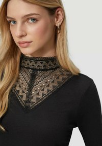 Zwarte top met een hoge kanten kraag met geometrische patronen en transparante details, in contrast met een textuur van zwarte stof.