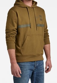 Sudadera con capucha de color verde oliva con dos rayas horizontales y un bolsillo frontal, que presenta una textura suave y puños y dobladillo acanalados.