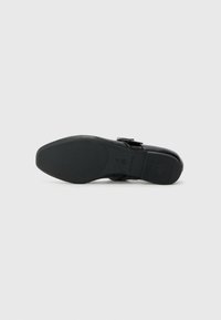 Chaussure noire avec une tige en cuir lisse, un accent de boucle et une semelle en caoutchouc texturé avec grip, vue par le dessous.